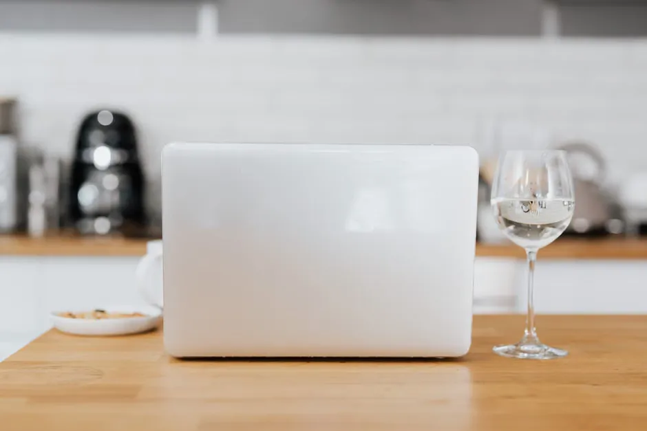 Kitchen table with a laptop, payslips and a pen in morning window light