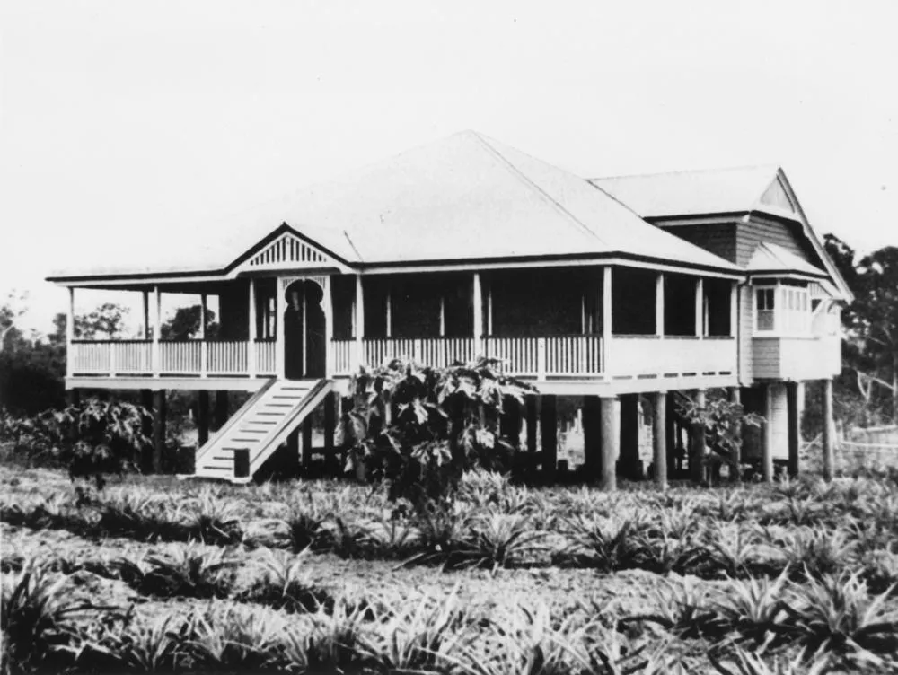 Weatherboard Queenslander house with a for sale sign on the front fence